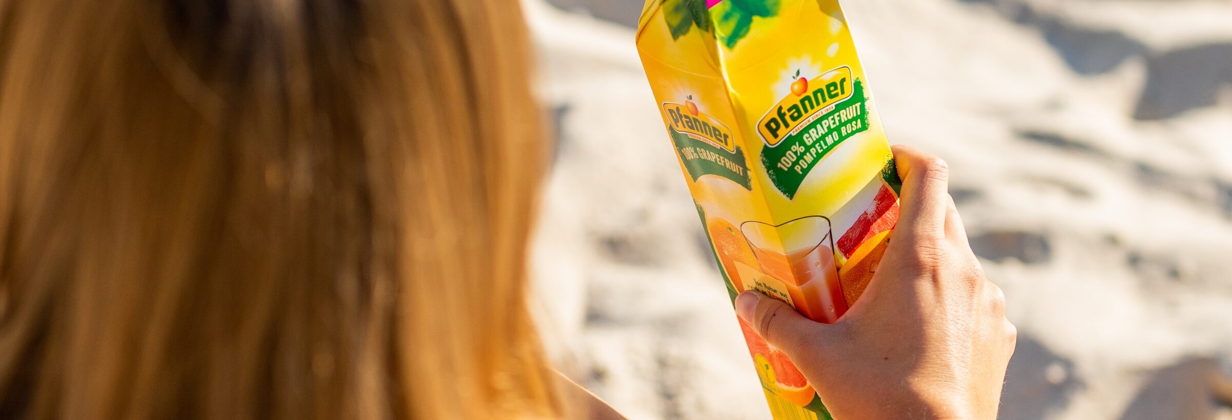 Frau am Strand mit einer Packung Pfanner 100 % Grapefruitsaft